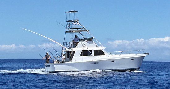 White sport fishing boat cruising on the blue ocean with anglers on board under a sunny sky