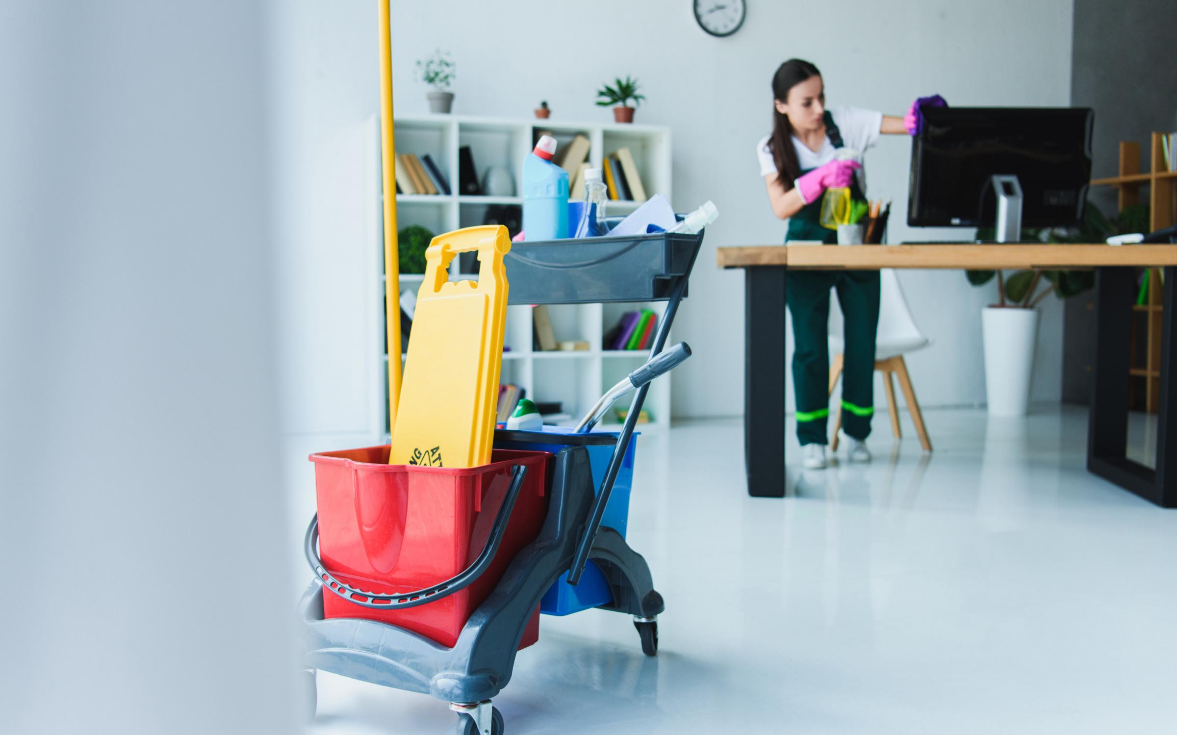 Janitorial Cleaning Services professional cleaning an office workspace with cleaning cart and supplies