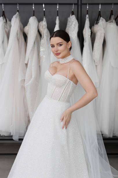 Beautiful young woman bride tries on a white wedding dress against the background of a large number of dresses in the store. Beautiful young woman bride tries on a white wedding dress against the background of a large number of dresses in the store Milanova Bridal dress stock pictures, royalty-free photos & images